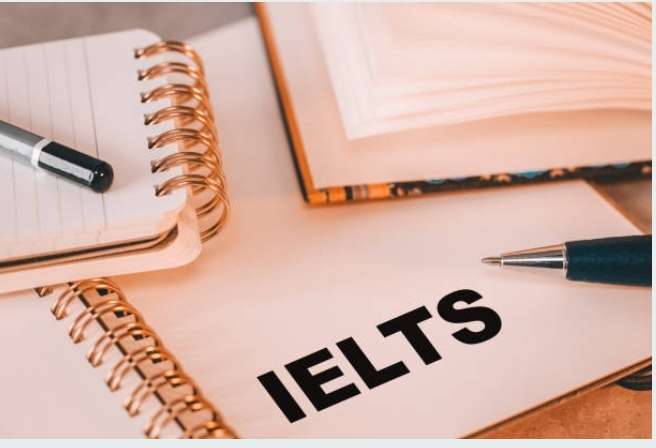Close-up of a study desk with an open notebook displaying the word IELTS, a black pen, and other books, symbolising preparation for the exam