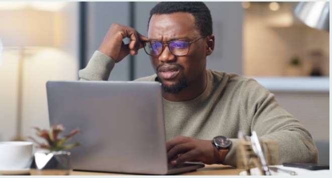 A man in glasses focused on his laptop, researching TEF and TCF exam difficulty.