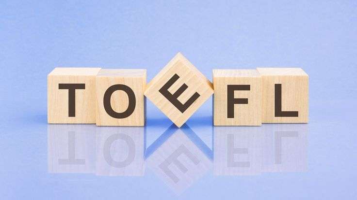 Wooden blocks spelling "TOEFL" on a reflective blue surface, with the letter "E" tilted.